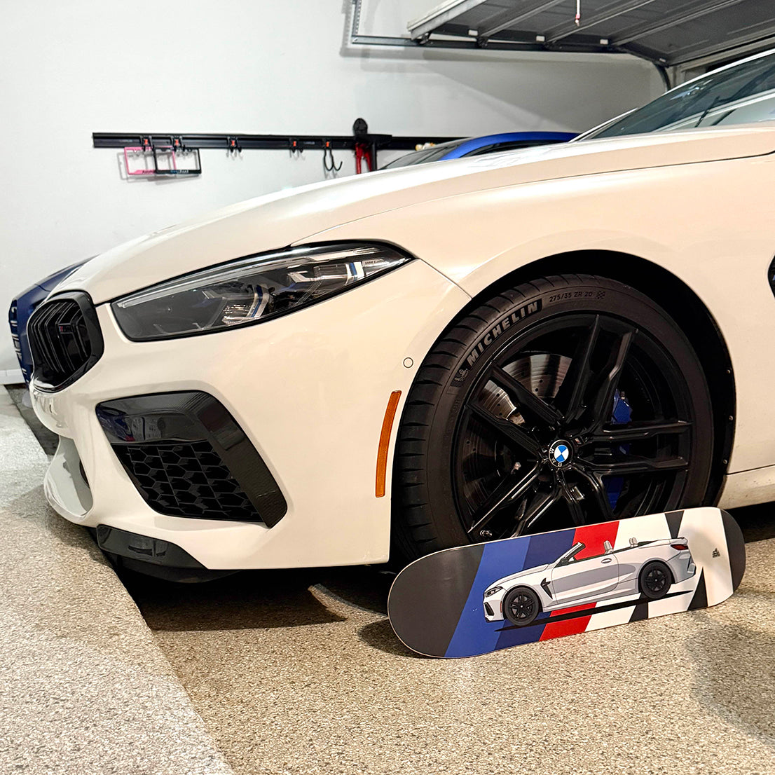 White BMW car in a garage with a skateboard featuring a car design in front of it.